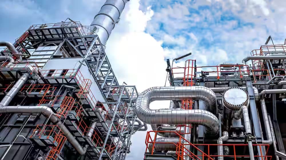 Industrial plant with insulated piping, steel structures, and safety walkways against a clear sky