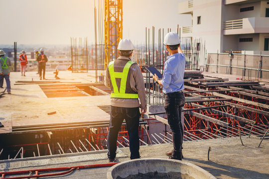 Engineers in hard hats reviewing construction progress on site with tablet and crane
