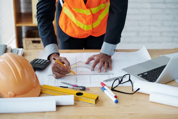 Engineer in hi-vis vest reviewing insulation drawings on blueprints at a planning desk