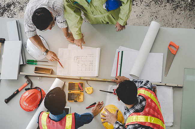 Project team reviewing method statements and blueprints around a planning table